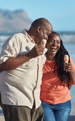 A couple smiling and hugging on the beach while eating an ice cream