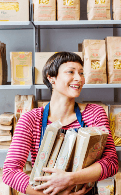 A smiling shopping assistant poses in front of shelves full of pasta boxes